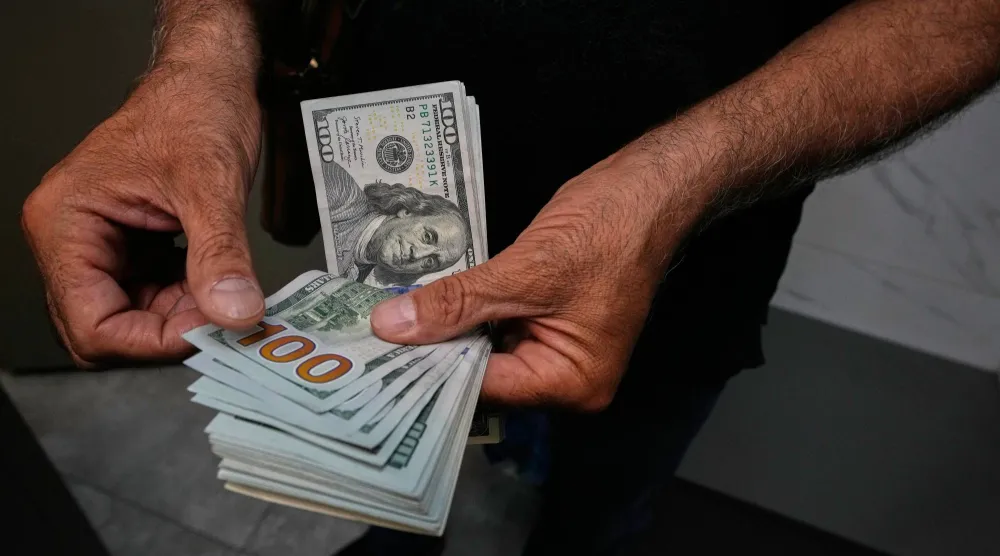 يقوم تاجر عملات بعدّ أوراق نقدية من فئة الدولار الأميركي في ساحة فردوسي بطهران (أ.ب)