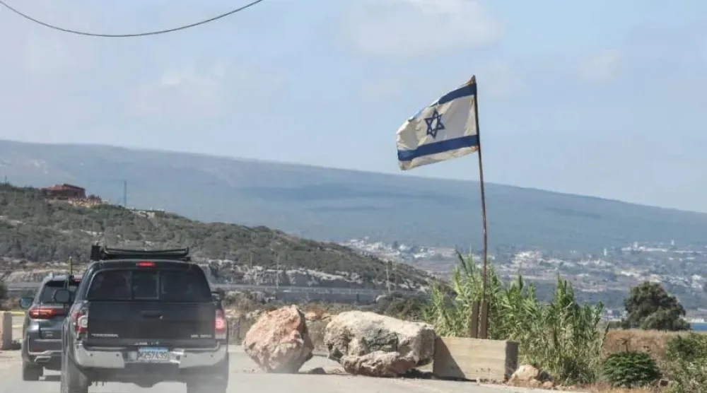 مدنيون من القرى المسيحية في جنوب لبنان يعبرون الطريق الساحلي جنوباً ضمن قافلة ويبدو العلم الإسرائيلي على مدخل بلدة الناقورة في يوليو 2026 (أرشيفية - أ.ف.ب)