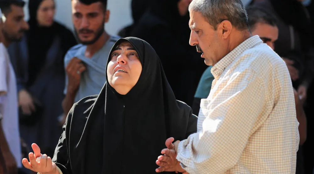 رجل يواسي امرأة ثكلى خلال جنازة فلسطينيين قُتلوا في غارات إسرائيلية في مدينة غزة يوم الأربعاء (رويترز)