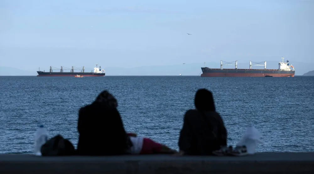 مواطنون يجلسون أمام سفن الشحن الراسية في بحر مرمرة في انتظار عبور مضيق البوسفور في إسطنبول (أ.ب)