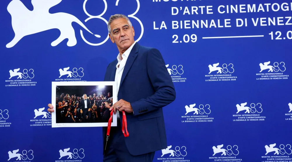 جورج كلوني يرفع صورة له من مهرجان البندقية السينمائي السابق خلال جلسة تصوير في الدورة الثالثة والثمانين لمهرجان البندقية السينمائي في البندقية - إيطاليا 2 سبتمبر 2026 (رويترز)