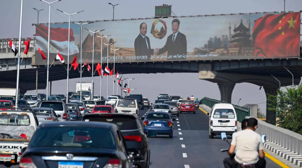 تمر سيارات أسفل شاشة عرض كبيرة تعرض صور الرئيس المصري عبد الفتاح السيسي ونظيره الصيني شي جينبينغ في القاهرة (أ.ف.ب)