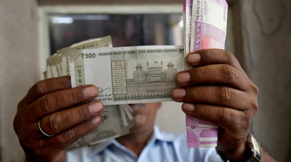 يتحقق أمين صندوق من أوراق نقدية بالروبية الهندية داخل غرفة بمحطة وقود في أحمد آباد (رويترز)