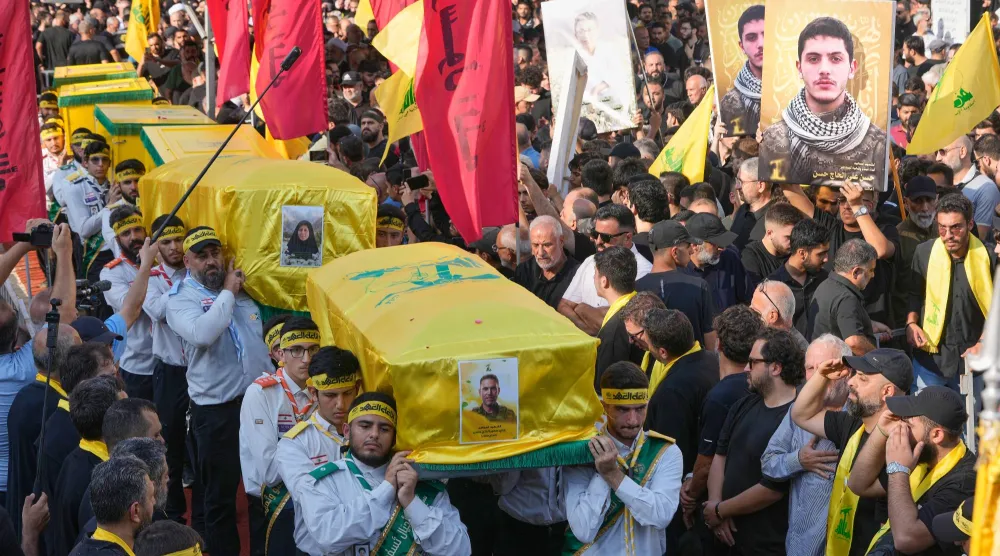 عناصر من كشافة «المهدي» يحملون نعوش قياديّ بـ«حزب الله» وعائلته خلال تشييعهم بالضاحية الجنوبية لبيروت (أ.ب)