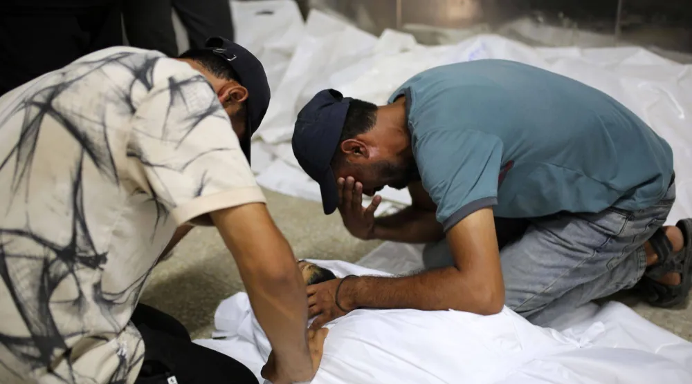 فلسطينيان يبكيان فوق جثمان آخر في مستشفى الشفاء بمدينة غزة يوم الخميس بعد مقتله في غارة إسرائيلية (د.ب.أ)