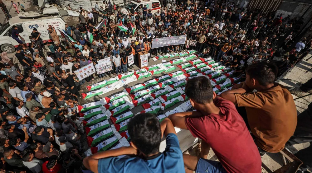 تَجمَّع المشيّعون في مدينة غزة لدفن جماعي لنحو 100 فلسطيني بينهم 62 طفلاً انتُشل رفاتهم من تحت الأنقاض (أ.ف.ب)