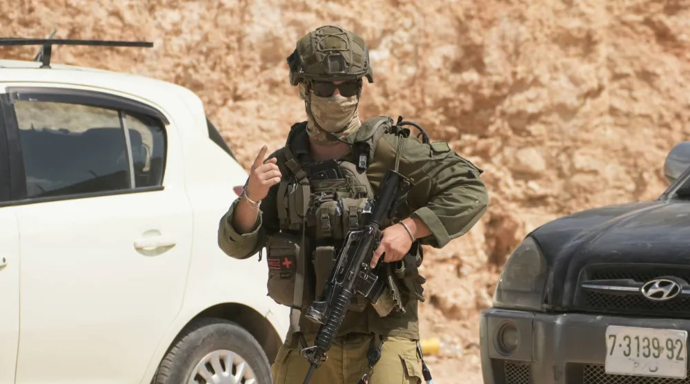 جندي إسرائيلي خلال هجوم مستوطنين على أملاك فلسطينيين في بلدة قصرة بالضفة الغربية يوم السبت (أ.ب)