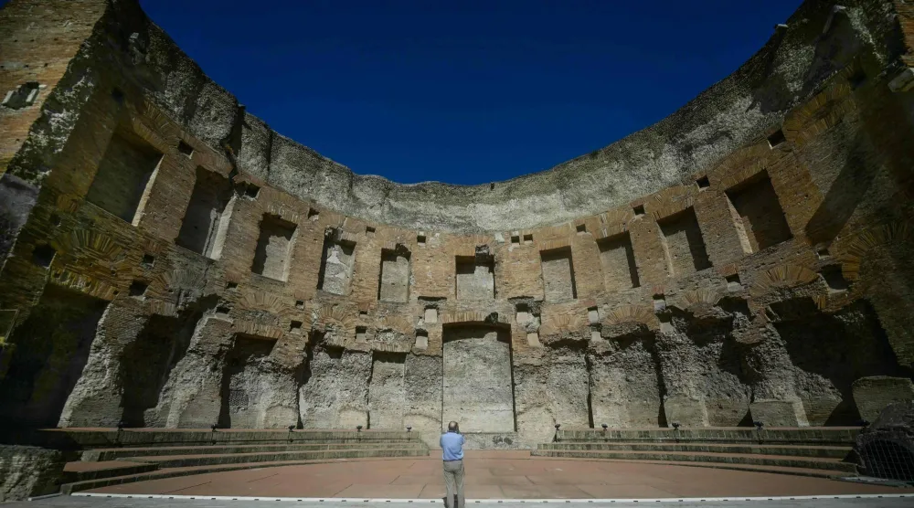 A visitor views the restored south-western exedra of the Baths of Trajan, a monumental second-century AD hall believed to have served as a library or space for public readings, with the Colosseum seen in the background, in Rome on September 8, 2026. (AFP)