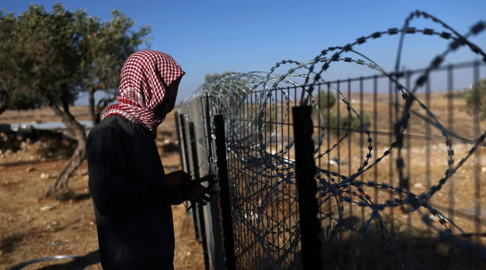 فلسطيني يعزز سياجاً حول بيته بقرية الطيبة في الضفة الغربية يوم الأربعاء لمنع هجمات المستوطنين (إ.ب.أ)