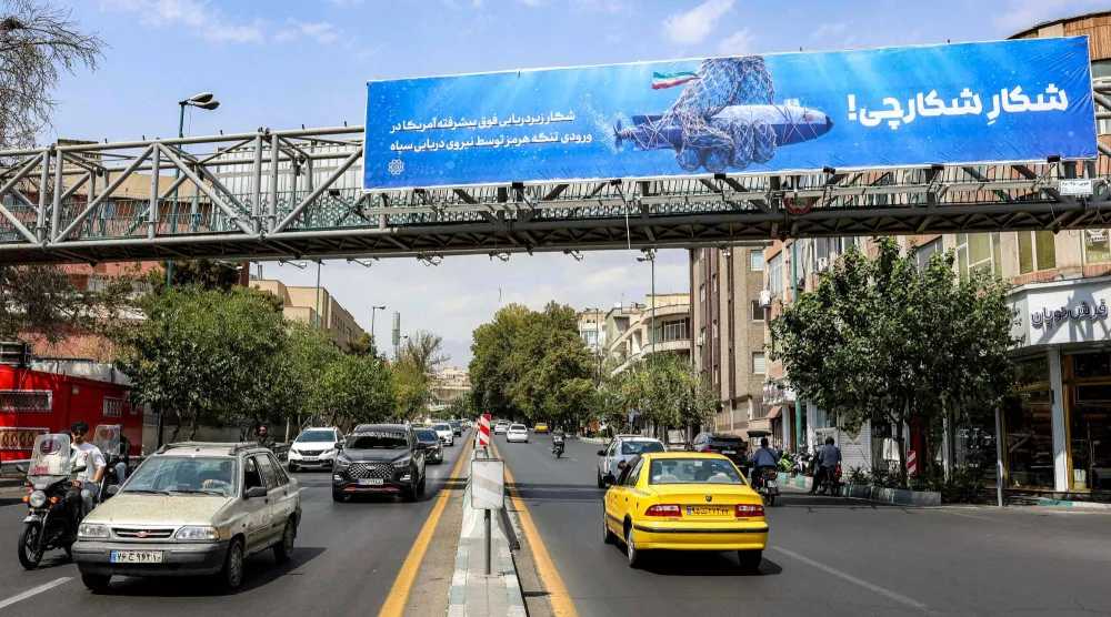 سيارات تتحرك على طول شارع بالقرب من جسر للمشاة يحمل لوحة إعلانية مناهضة لأميركا في طهران (أ.ف.ب)