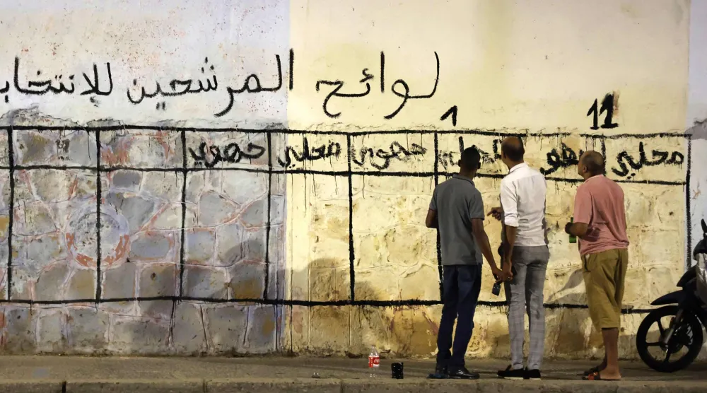 شُبان مغاربة أمام حائط خُصّص لحملة الانتخابات التشريعية (أ.ف.ب)