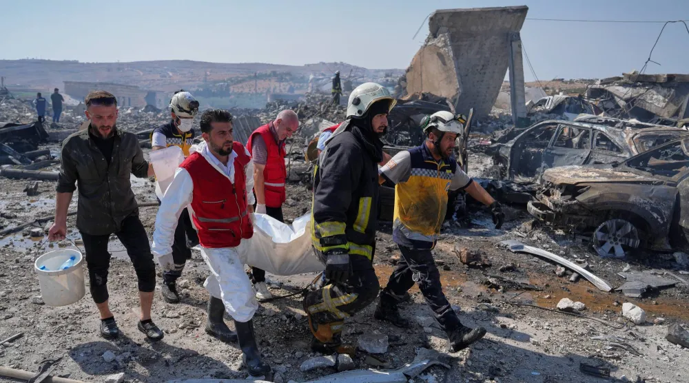 عناصر الدفاع المدني ورجل إطفاء ينتشلون جثة من موقع انفجار مستودع للتخزين المؤقت للأسلحة بالقرب من سرمدا بمحافظة إدلب الأربعاء (أ.ب)