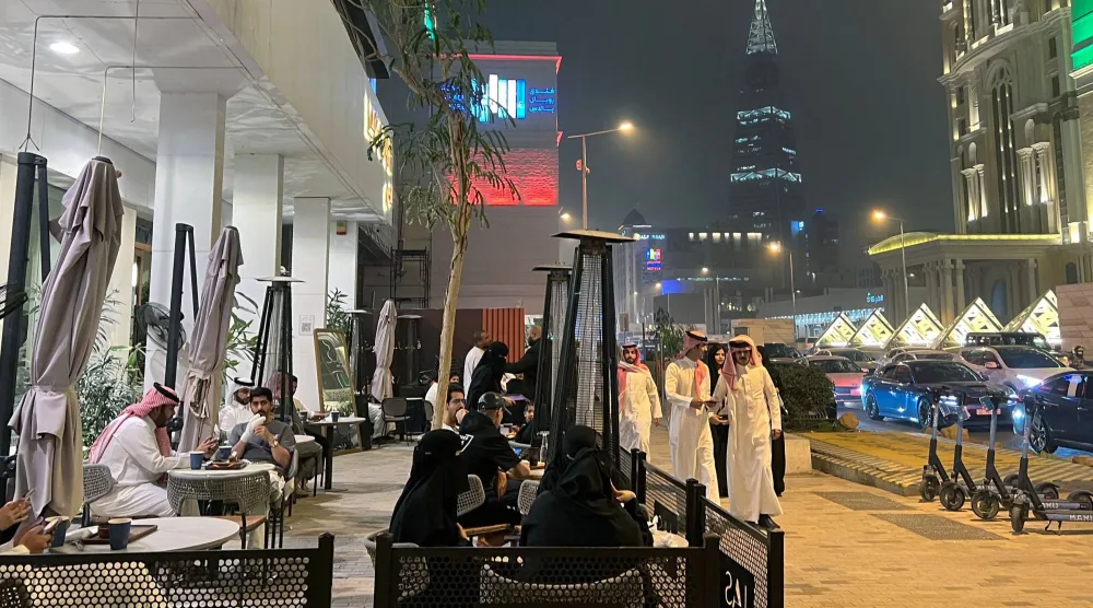 يمر الناس أمام مقهى على طول شارع التحلية التجاري في الرياض (أ.ف.ب)