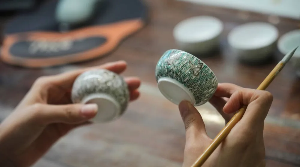 Chinese porcelain artist Chen Qing holds up two cups after painting them in Jingdezhen, known as China's "Porcelain Capital," in eastern China's Jiangxi province, Tuesday, Sept. 1, 2026. (AP Photo/Achmad Ibrahim)
