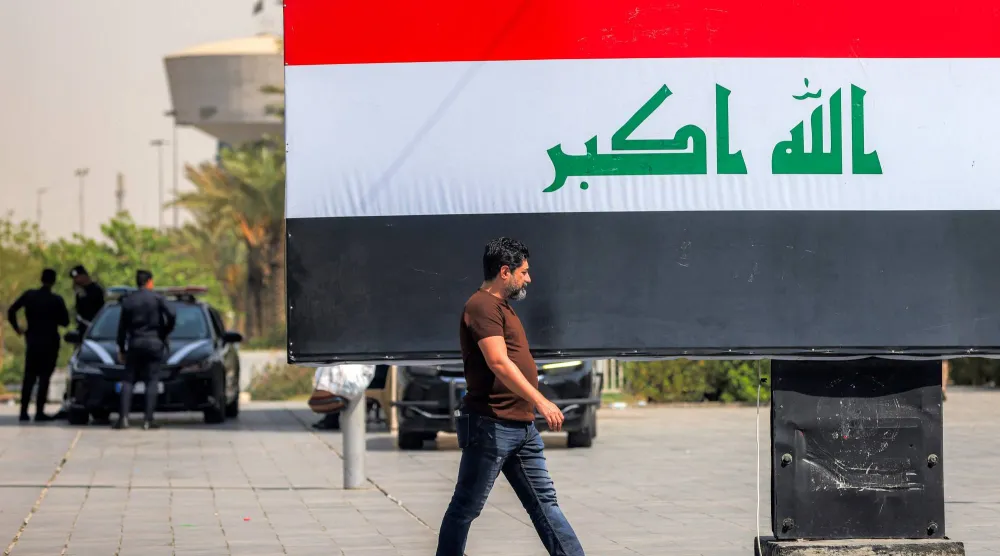 عراقي يمر أمام لوحة إعلانية تحمل العلم العراقي في ساحة التحرير بوسط بغداد في 22 سبتمبر 2026 (أ.ف.ب)