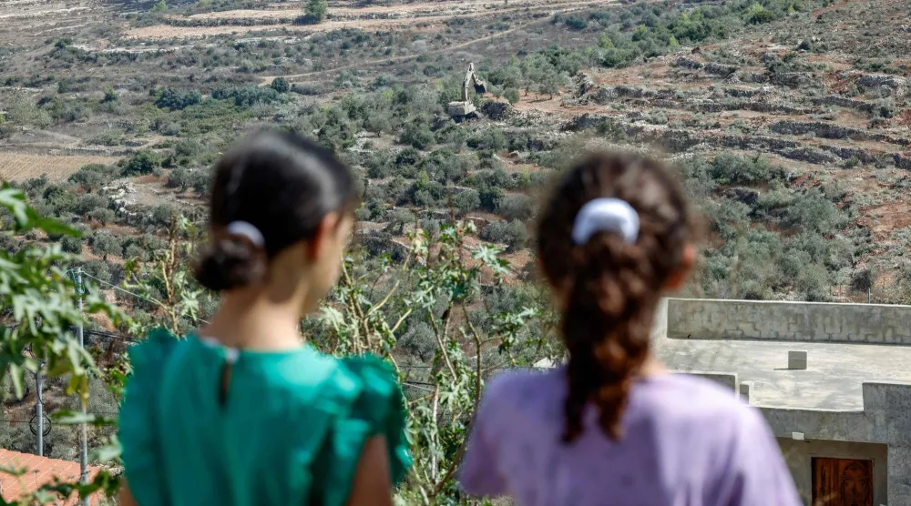 فتيات فلسطينيات يشاهدن جرافة إسرائيلية تقتلع أشجار الزيتون في قرية دير نظام شمال غرب رام الله في الضفة الغربية المحتلة (أ.ف.ب)