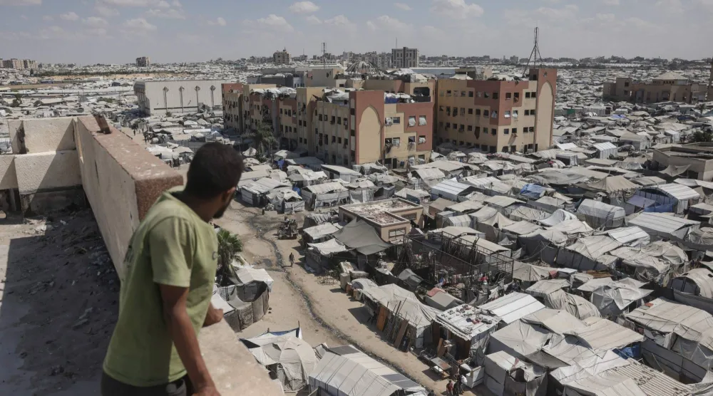 رجل يقف فوق مبنى ينظر إلى خيام فلسطينيين نازحين في منطقة المواصي بخان يونس في جنوب قطاع غزة (أ.ف.ب)