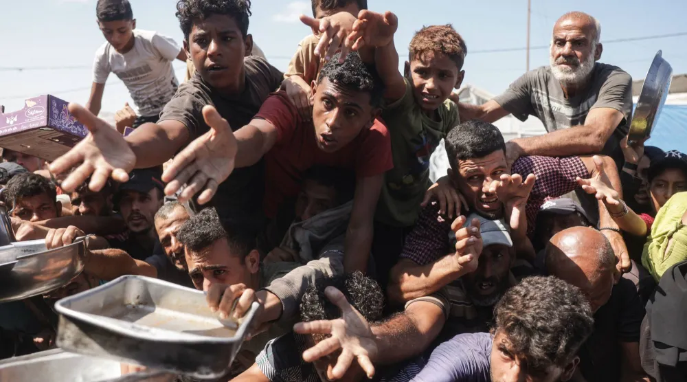فلسطينيون نازحون ينتظرون للحصول على وجبة طعام في مطبخ خيري بخان يونس يوم الجمعة (أ.ف.ب)