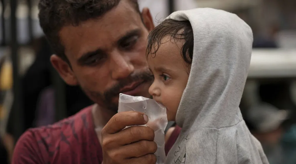 فلسطيني يعطي طفلاً شربة ماء من كيس اشتراه بشيقل في أجواء بالغة الحرارة بمدينة غزة أغسطس 2025 (أ.ب)