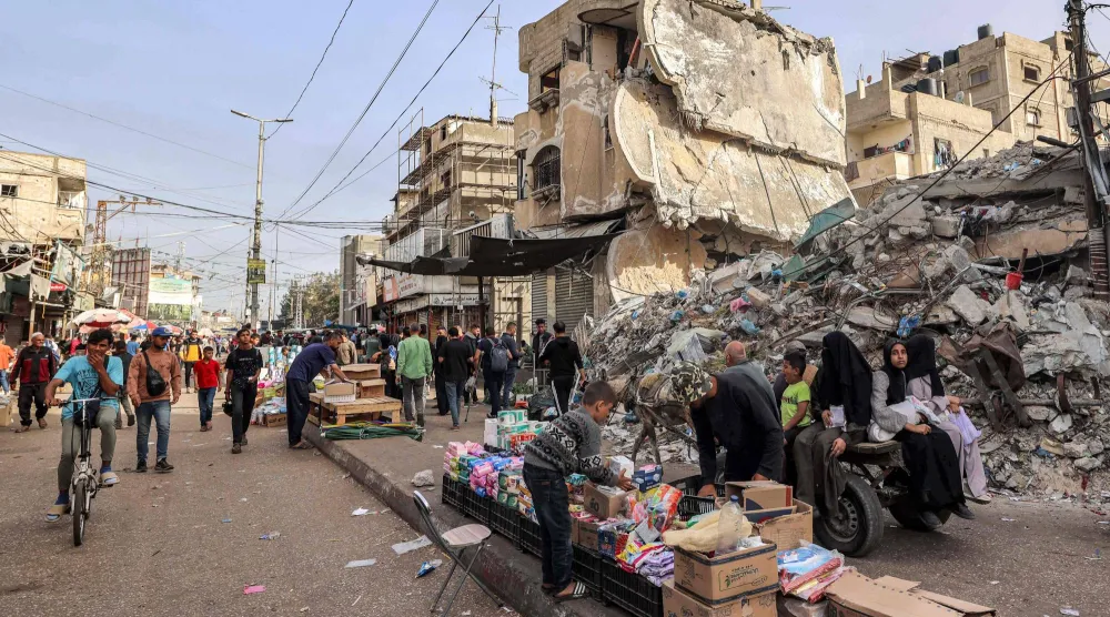 صبي يساعد بائعاً في ترتيب بضائعه خلال وقوفه أمام أنقاض مبنى منهار في رفح جنوب قطاع غزة أبريل 2024 (أ.ف.ب)
