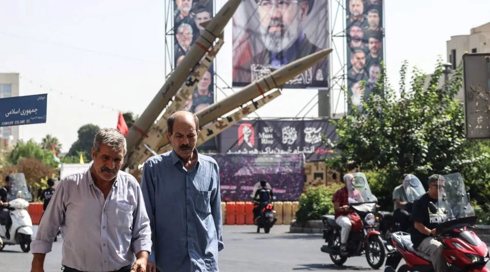 رجال إيرانيون يمرون بجوار صواريخ معروضة بجانب صورة كبيرة للمرشد الإيراني مجتبى خامنئي في ساحة بهارستان في طهران يوم 28 سبتمبر 2026 (أ.ف.ب) 