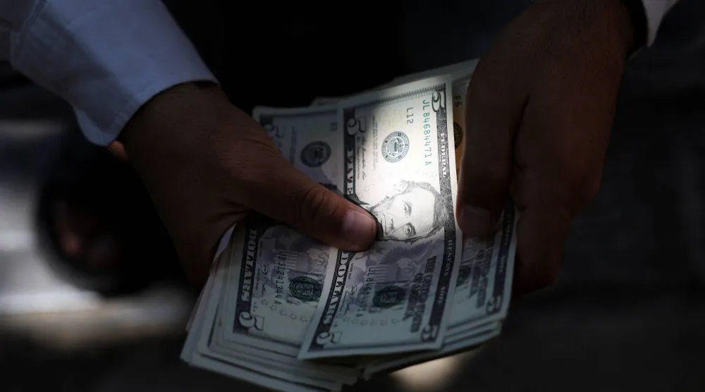 تاجر عملات يحمل أوراقًا نقدية من فئة الدولار الأميركي في طهران (رويترز)