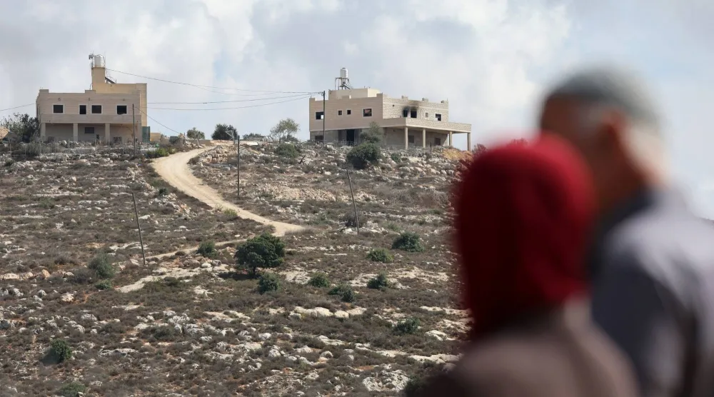 الفلسطيني محمود الطوباسي (60 عاماً) وزوجته عايدة (51 عاماً) يقفان بمنطقة تطل على منزلهما الذي تضرر جراء هجوم شنه مستوطنون إسرائيليون في جالود بالضفة الغربية المحتلة الثلاثاء (رويترز)