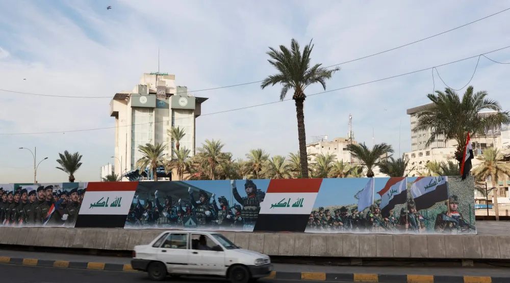 سيارة تمر بجوار لافتة تحمل صوراً للأعلام العراقية وقوات الأمن بمناسبة «يوم السيادة» في بغداد (رويترز)