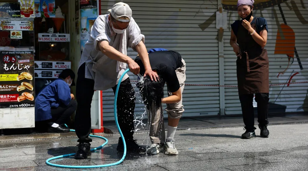 عامل بمطعم وجبات سريعة يحاول تبريد شخص برشّ الماء على رأسه خلال موجة حر شديدة بطوكيو 22 يوليو 2026 (رويترز)