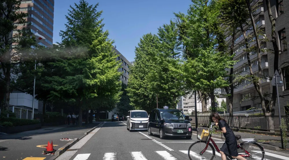 This picture taken on August 25, 2026 shows a woman crossing with her bike on a street in Tokyo. (Photo by Philip FONG / AFP)