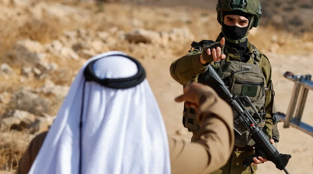 عنصر من القوات الإسرائيلية يشير بيده إلى فلسطيني أثناء قيامه بأعمال الحراسة خلال هدم مبنى فلسطيني بالقرب من الخليل في الضفة الغربية التي تحتلها إسرائيل (رويترز)