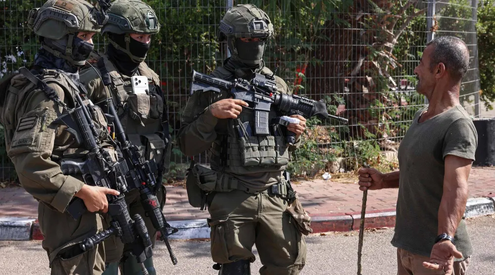 مزارع فلسطيني يتحدث مع جنود إسرائيليين خلال موسم الحصاد في كروم الزيتون الفلسطينية بقرية رنتس قرب رام الله في الضفة الغربية المحتلة (أ.ف.ب)
