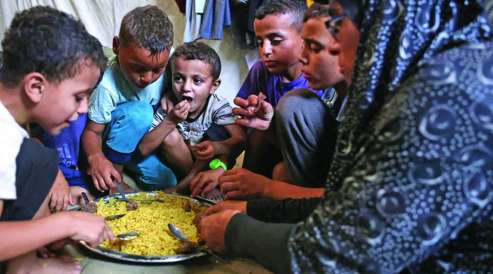 
نازحة فلسطينية من بيت حانون تتقاسم مع أطفالها طعاماً حصلت عليه من مطبخ خيري في خان يونس جنوب قطاع غزة أمس (أ.ف.ب)