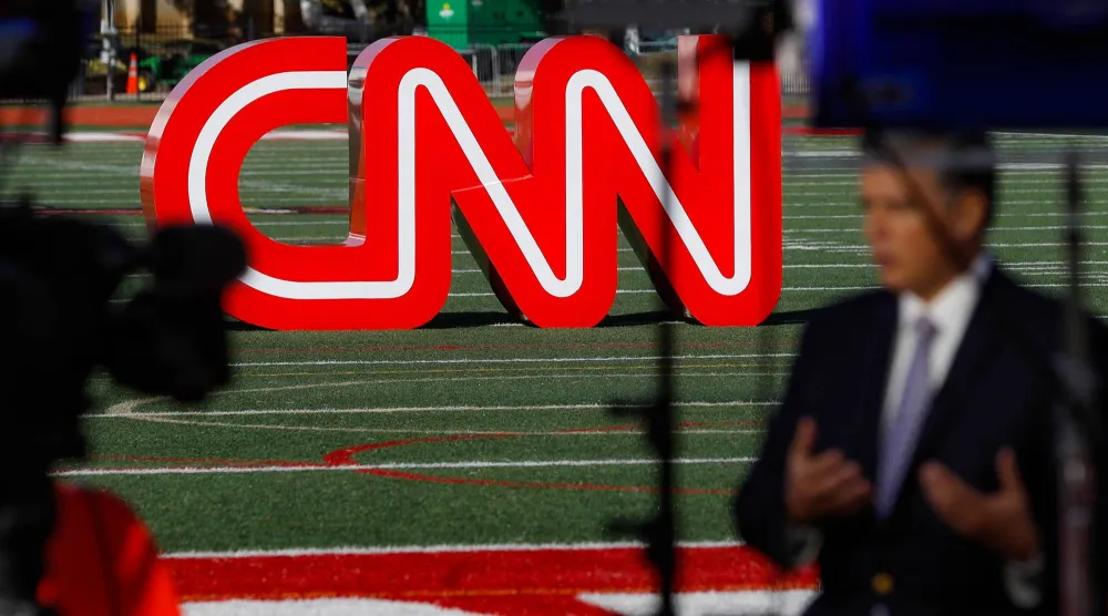 صحفي يسجل مقطع فيديو بالقرب من لافتة لشبكة "سي إن إن" (CNN) (أ.ب)