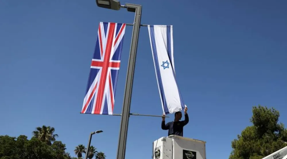 عامل في بلدية القدس يعلّق العلم الإسرائيلي بجوار العلم البريطاني بالقرب من مقر الرئاسة الإسرائيلية في القدس 25 يونيو 2018 (رويترز)