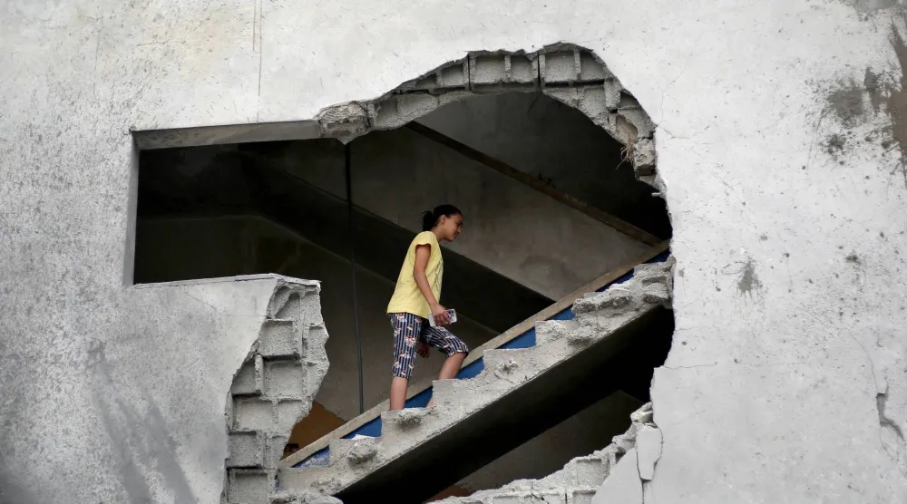 فتاة فلسطينية تصعد درجاً في مبنى مدمر استُهدف بغارات جوية إسرائيلية بمنطقة الزوايدة وسط قطاع غزة الأحد (أ.ف.ب)