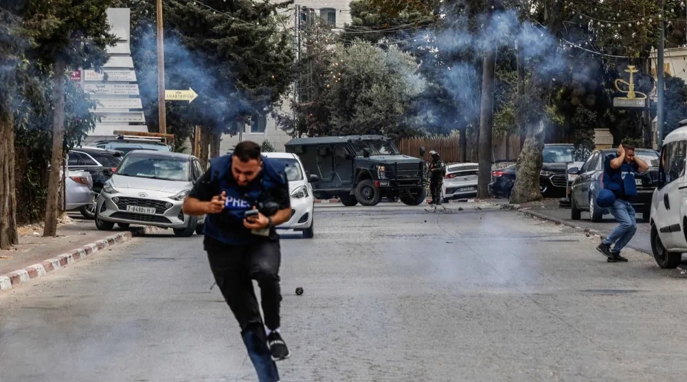 صحافيون يفرون من قنابل غاز أطلقتها قوات الجيش الإسرائيلي في أثناء مداهمة في رام الله بالضفة الغربية الثلاثاء (أ.ف.ب)