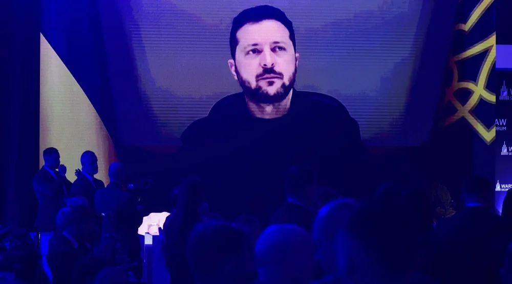 أشخاص يتابعون الرئيس الأوكراني فولوديمير زيلينسكي عبر شاشة كبيرة خلال كلمته أمام منتدى وارسو للأمن في العاصمة البولندية وارسو يوم 12 أكتوبر 2026 (أ.ب)