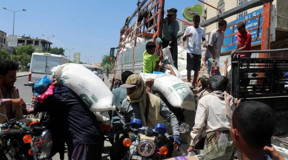 أشخاص ينقلون دقيق القمح من على متن شاحنة في تعز المحاصرة من قبل الحوثيين (رويترز)
