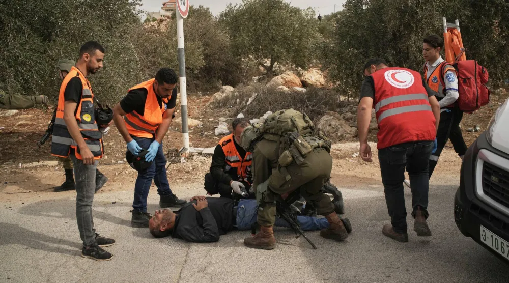 مسعفون فلسطينيون يعاينون رجلاً أصابه رصاص إسرائيلي في الضفة الغربية بعد اعتداء مستوطنين على قاطفي الزيتون في قرية خربة أبو فلاح (أ.ب)