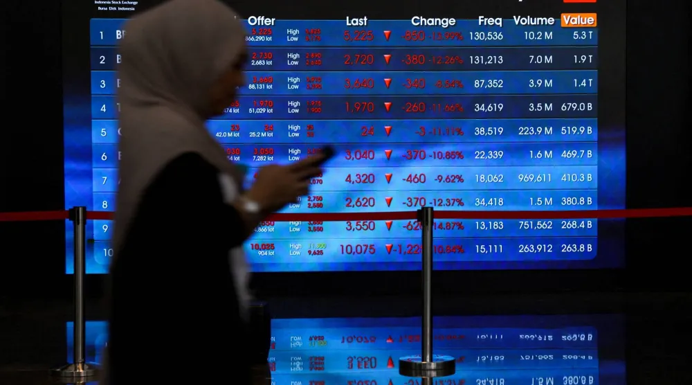 عاملة تمرّ أمام لوحة إلكترونية تعرض تحركات الأسهم ببورصة إندونيسيا في جاكرتا (رويترز)
