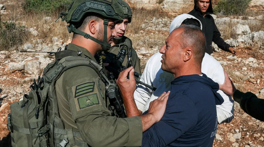 رجل فلسطيني يتحدث مع القوات الإسرائيلية بينما تقوم هذه القوات باحتجاز فلسطيني آخر وذلك خلال موسم قطف الزيتون في بساتين زيتون يملكها فلسطينيون في دير أبو مشعل بالقرب من رام الله في الضفة الغربية (رويترز)
