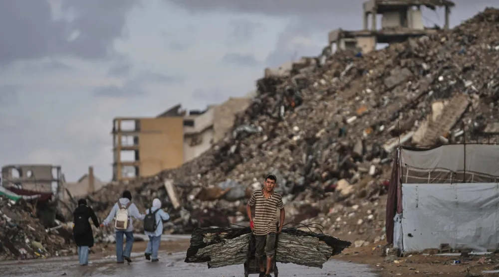 فلسطيني يحمل ألواحاً معدنية يمر بأطلال مبانٍ دُمرت خلال الحرب يوم الأحد (أ.ب)