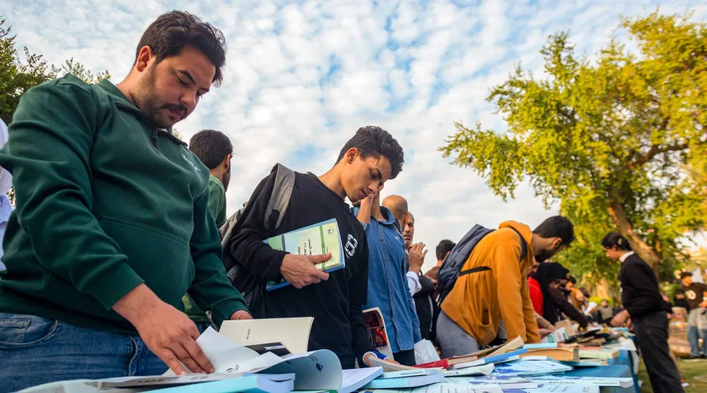 عراقيون يعاينون كتباً معروضة بشارع أبو نواس وسط بغداد ضمن فعالية «أنا عراقي أنا أقرأ» حيث وزع 30 ألف كتاب مجاناً (أ.ف.ب)