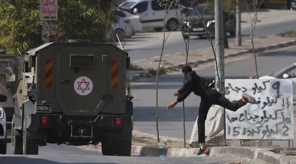 فلسطيني يرشق بالحجارة سيارة لجيش الاحتلال الإسرائيلي في مخيم بلاطة للاجئين قرب نابلس في الضفة الغربية المحتلة يوم الأربعاء (إ.ب.أ)