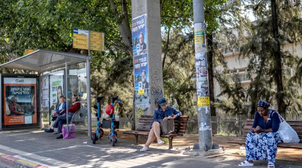 İsrailliler, salı günü Tel Aviv’in güneyinde, üzerlerinde aşırı sağcı Yahudi Gücü Partisi’nin seçim afişlerinin bulunduğu bir otobüs durağında beklerken (AFP)