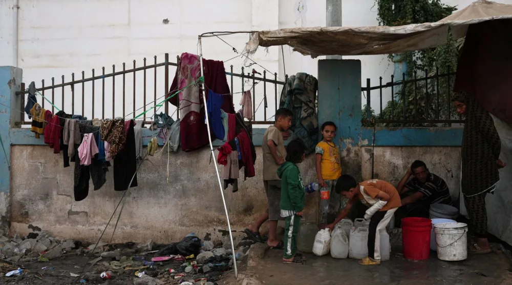 فلسطينيون يملأون عبوات بلاستيكية ماءً في دير البلح بغزة (أ.ب)