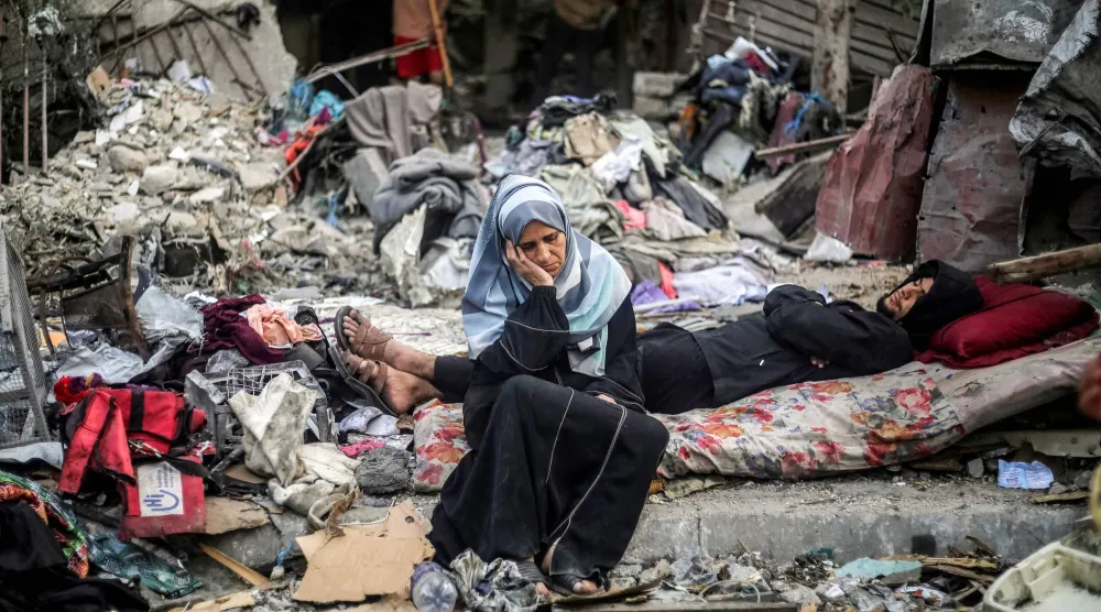 فلسطينية قرب رجل مستلقٍ على فرشة وسط الدمار بعد غارة جوية إسرائيلية في النصيرات وسط قطاع غزة الجمعة (أ.ف.ب)