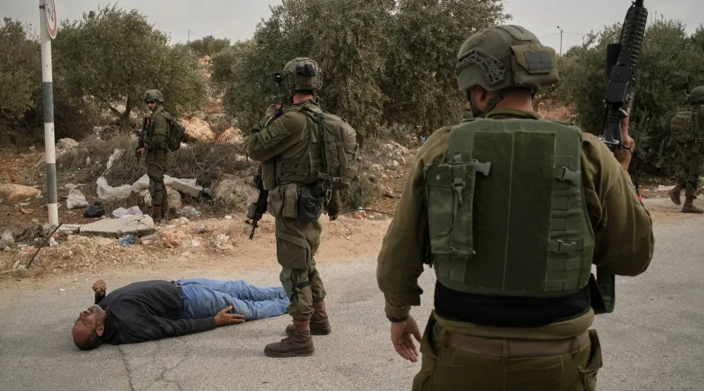 جنود إسرائيليون يقفون بجانب رجل فلسطيني جريح في أعقاب هجوم مستوطنين على فلسطينيين يقطفون الزيتون في الضفة الغربية (أ.ب)