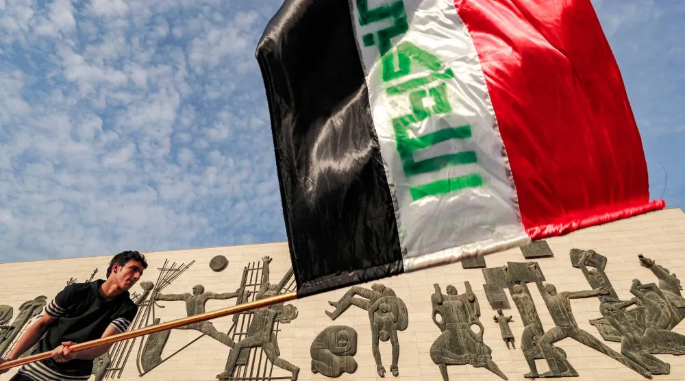 رجل يلوّح بالعلم العراقي في ساحة التحرير ببغداد (أ.ف.ب)